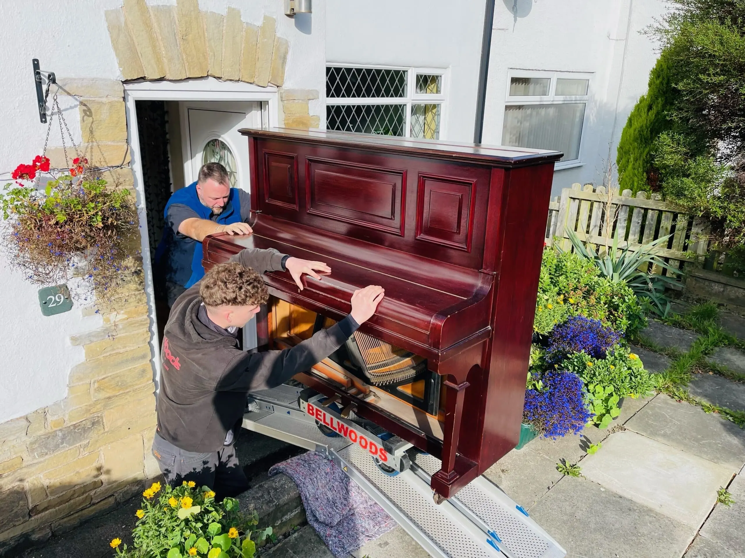 Bellwoods Removals team moving a mahogany upright piano through a front doorway using specialist skate equipment — piano removals across West Yorkshire
